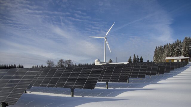 Solar Panels On Snow With Windmill Under Clear Day Sky